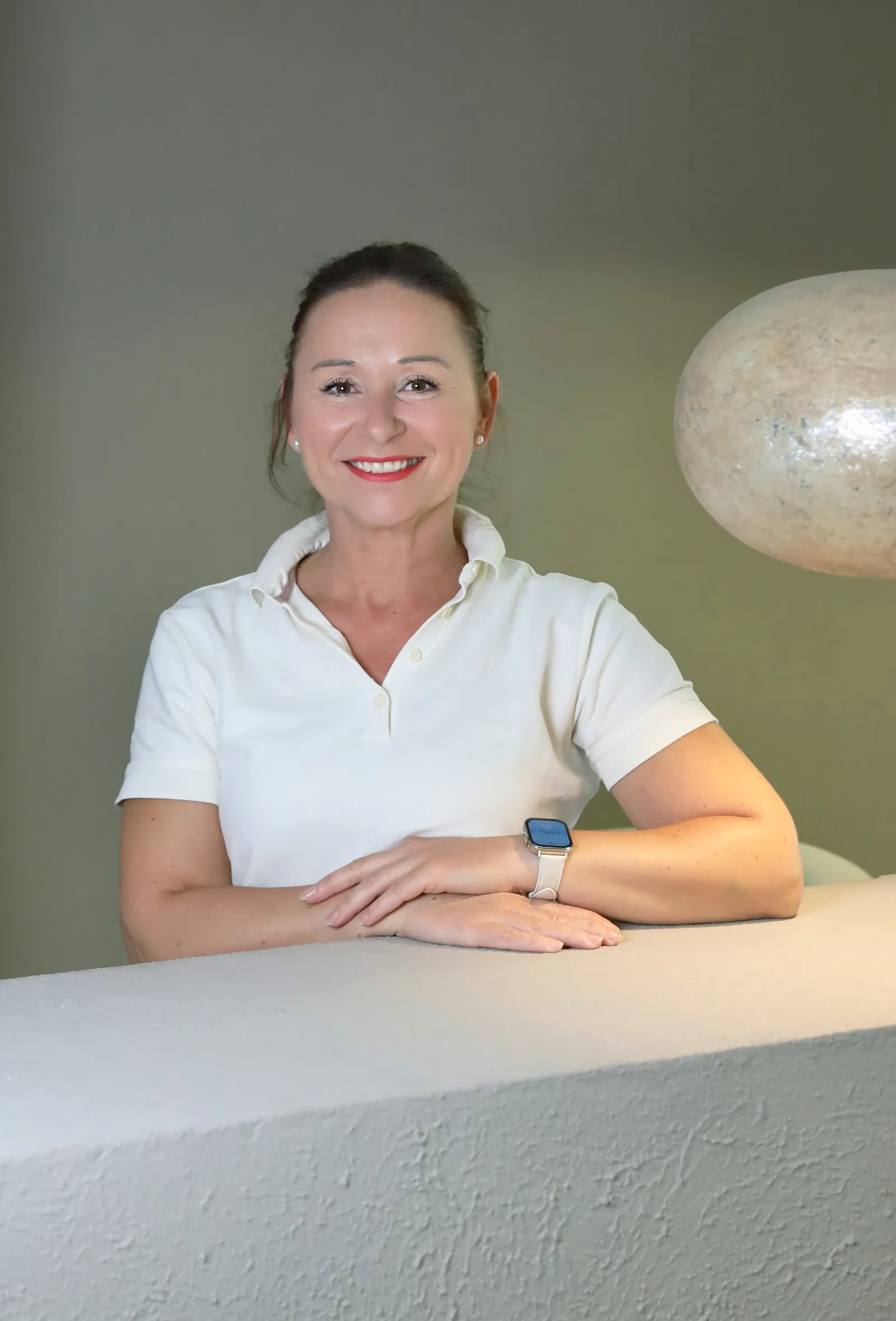 Olimpia Nordgren lehnt an einem verputzten Tisch, im Hintergrund eine skulpturale Pendelleuchte